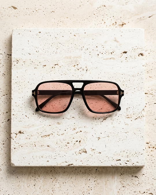 Iris Frames Riviera sunglasses in black frame with rose tinted lenses on travertine stone surface