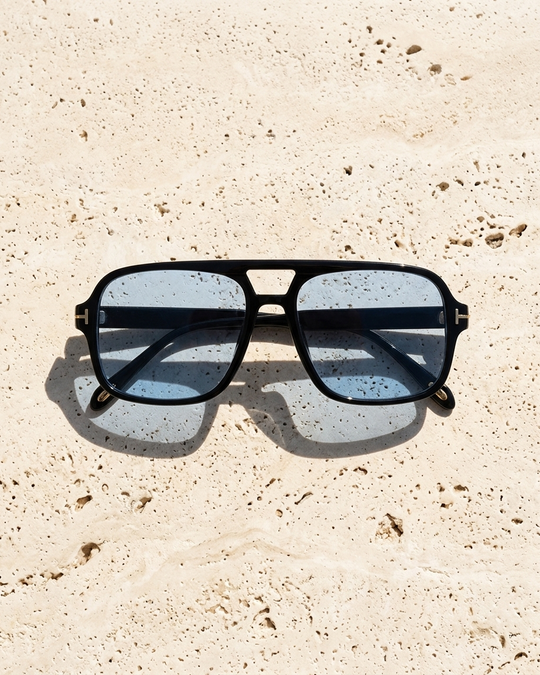 Iris Frames Riviera sunglasses in black frame with amber yellow tinted lenses on white stone surface