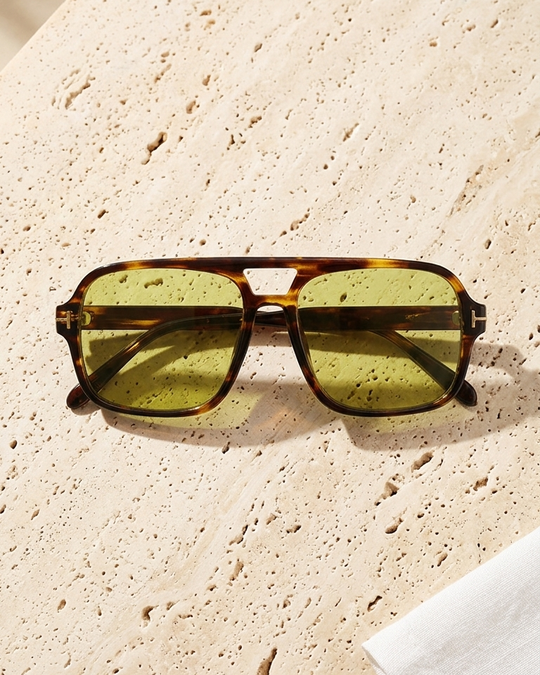 Iris Frames Riviera sunglasses in tortoise frame with olive green tinted lenses on travertine stone